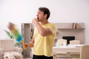 A man sneezing as he dusts a house.